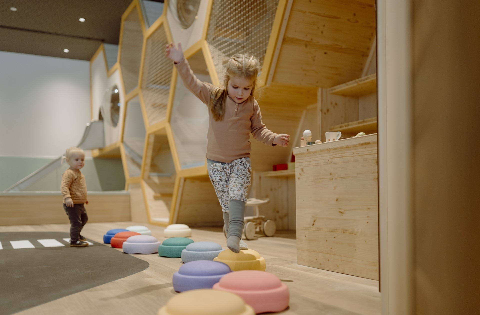 Kinder erkunden einen kreativen Spielbereich mit bunten Ringen und Holzdetails.