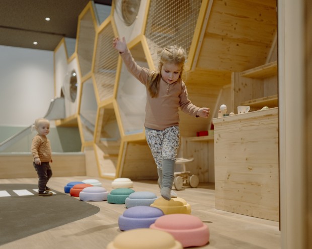 Kinder erkunden einen kreativen Spielbereich mit bunten Ringen und Holzdetails.