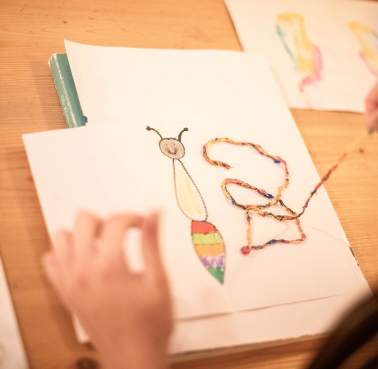 Ein Kind malt ein Tiermotiv auf einem Holzbrett mit bunten Farben.