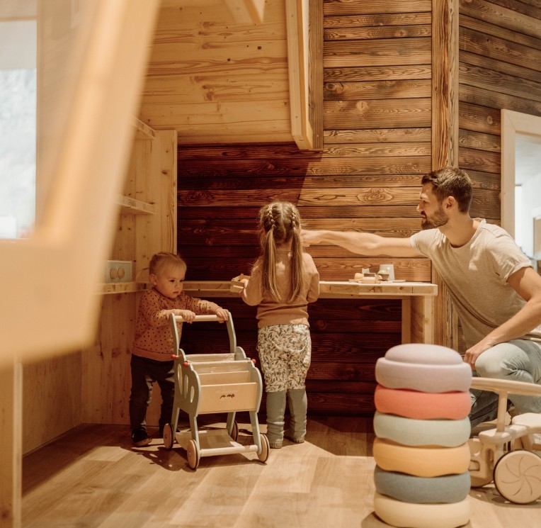 Kinder spielen in einer Holzspielküche mit buntem Geschirr und Spielutensilien.