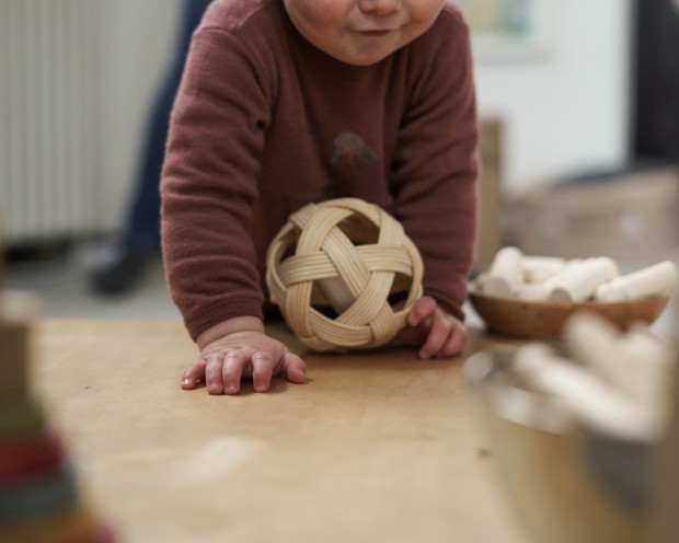 Ein Kleinkind spielt mit einem Holzball auf einer weichen Unterlage.