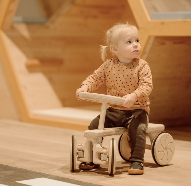 Ein kleines Kind spielt mit einem Holzauto in einer wabenförmigen Spielnische.