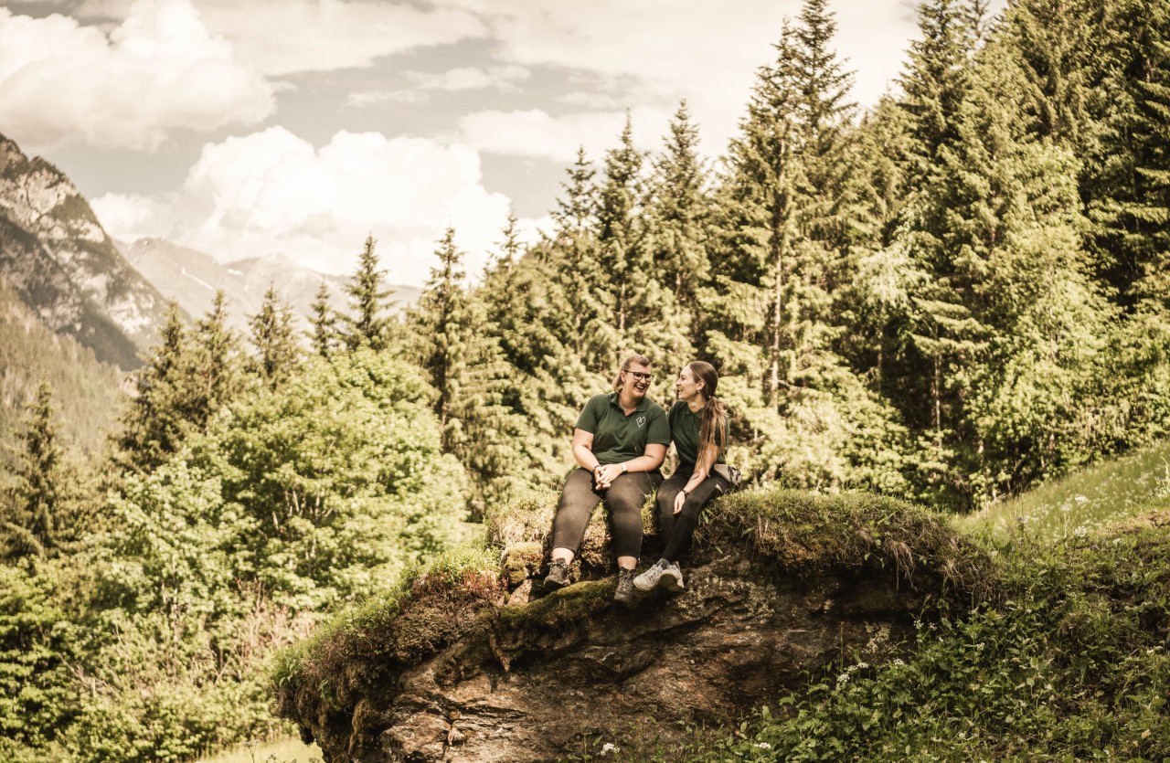 2 Reithelferinnen sitzen auf einem Stein im Wald