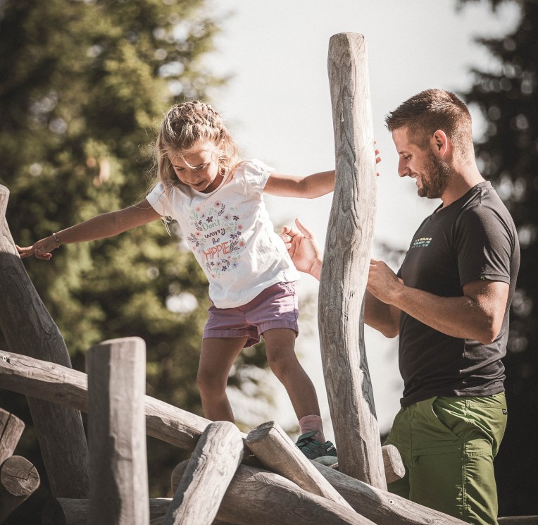 Vater hilft Kind beim Balancieren auf Baumstamm
