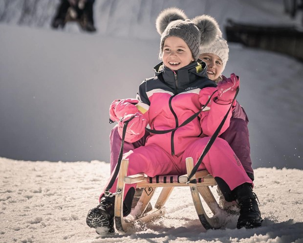 Schlittenfahren im Garten vom Familienhotel Feuerstein, dem idealen Ort für einen Familienurlaub in den Bergen