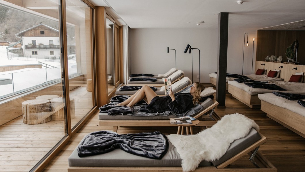 Frau liegt entspannt auf einer Liege und liest eine Zeitschrift