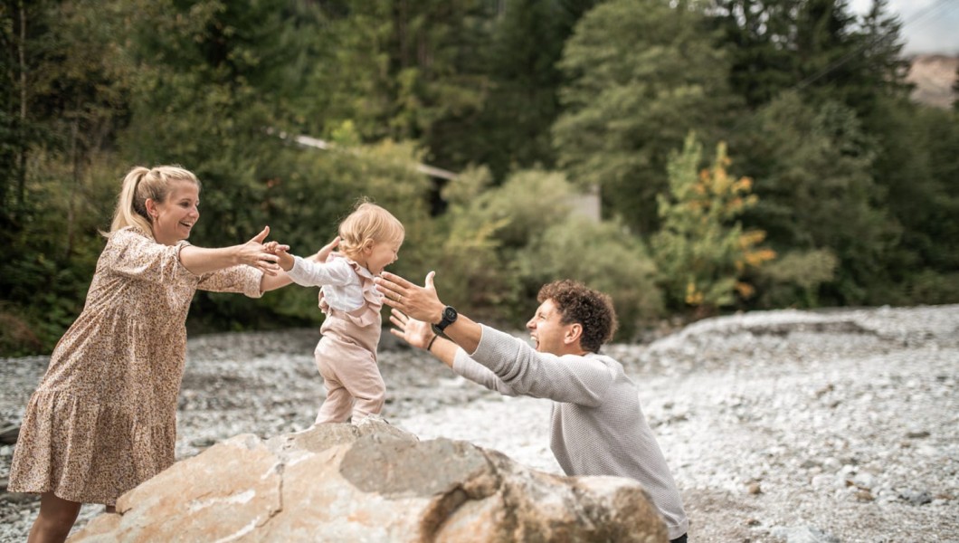 Kleines Kind geht auf einem Stein und Eltern halten sie fest