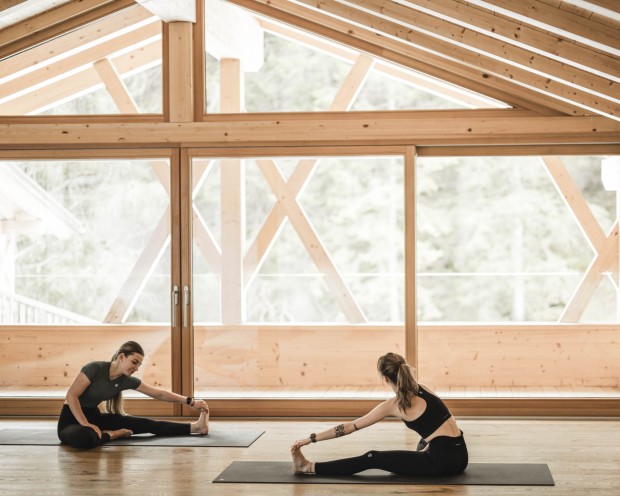 2 Frauen dehnen sich im Yoga Raum mit einem großen Fenster
