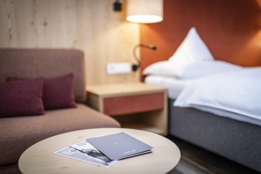 Kleiner runder Tisch mit Broschüren und im Hintergrund ein Bett und eine Couch