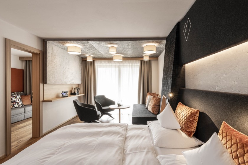 Doppelbett und am hinteren Ende des Zimmers eine Couch mit rundem Tisch und 2 Stühlen